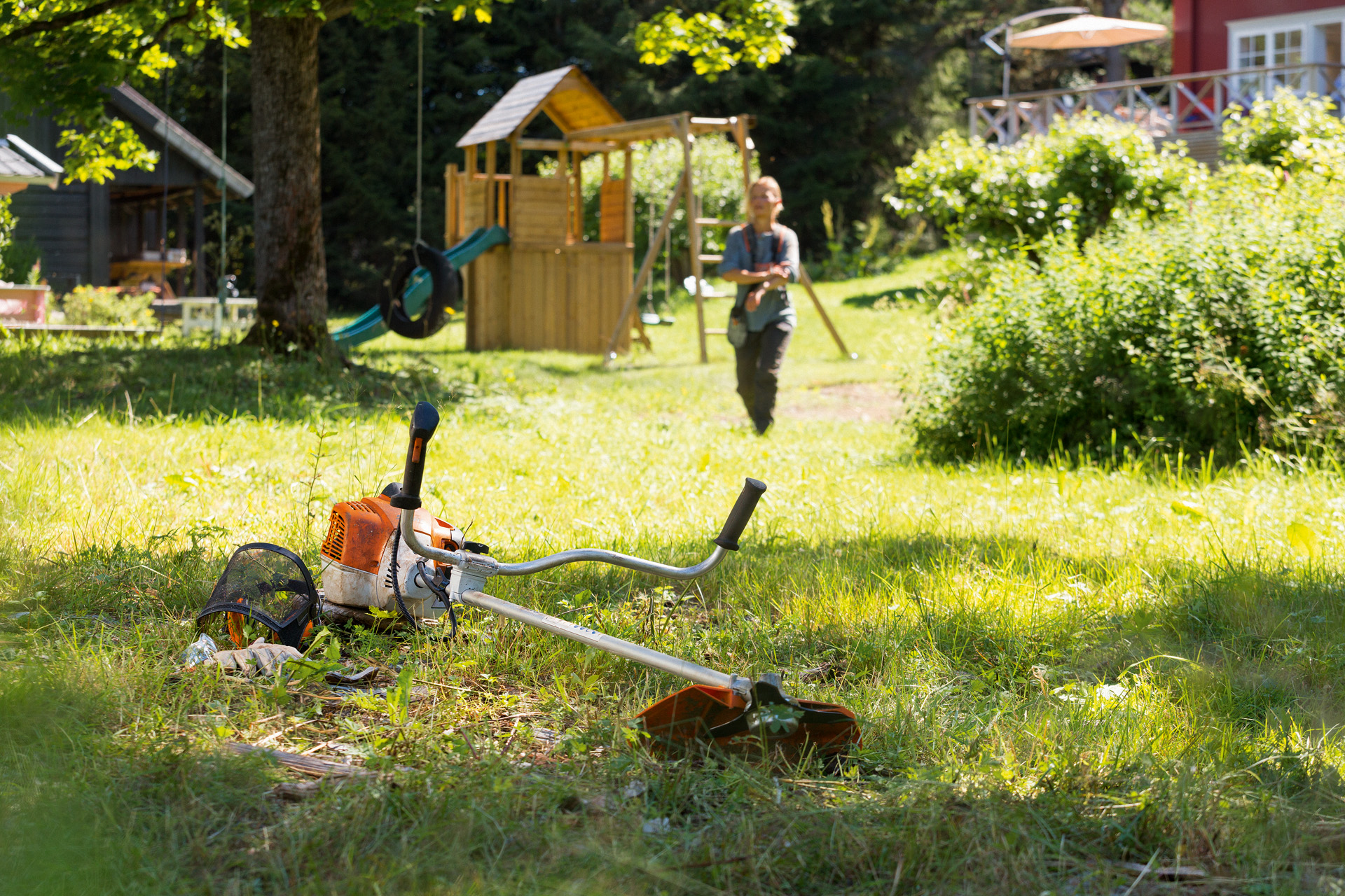 Una guadaña STIHL FS 240 sobre la hierba, en segundo plano un hombre se prepara para el mantenimiento