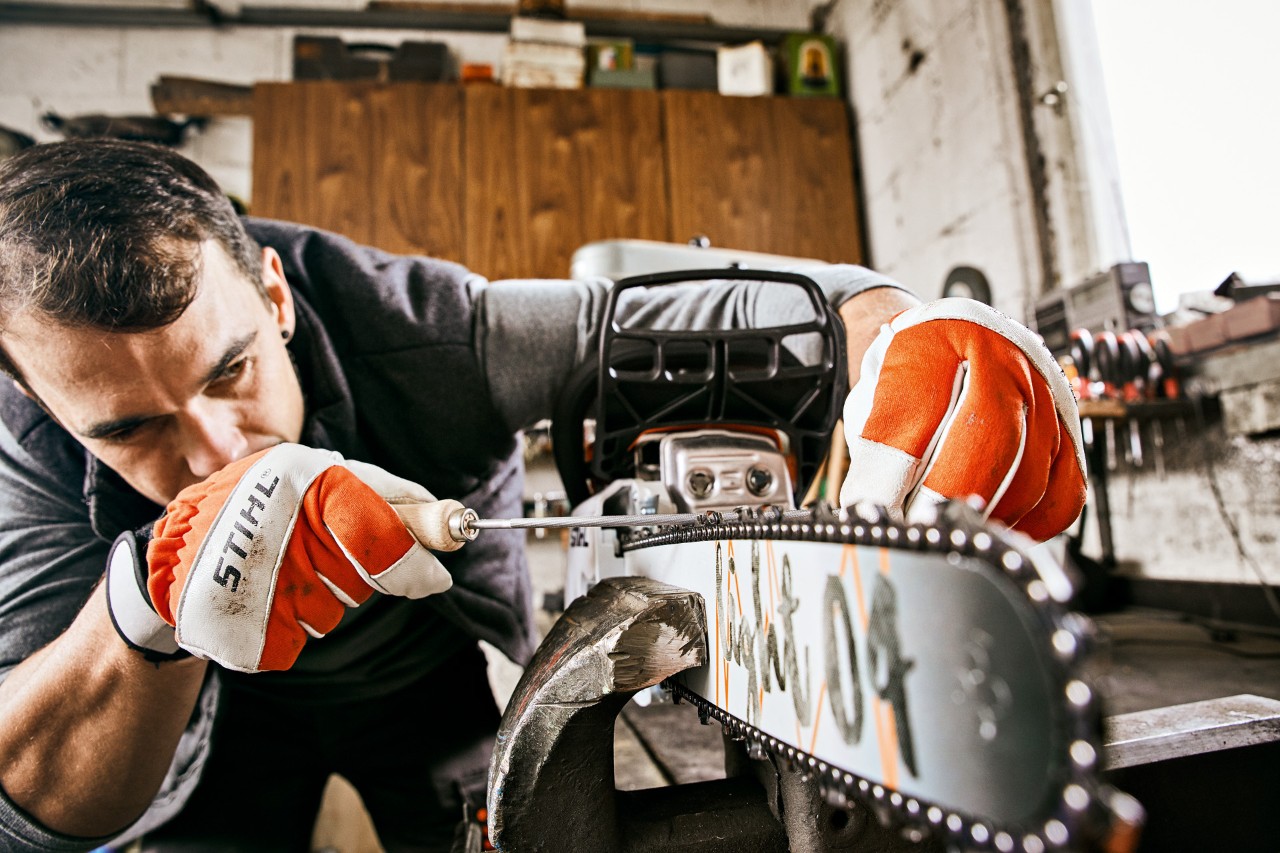 Un hombre con guantes STIHL afila la cadena de una motosierra de gasolina STIHL 261 C-M con una lima redonda