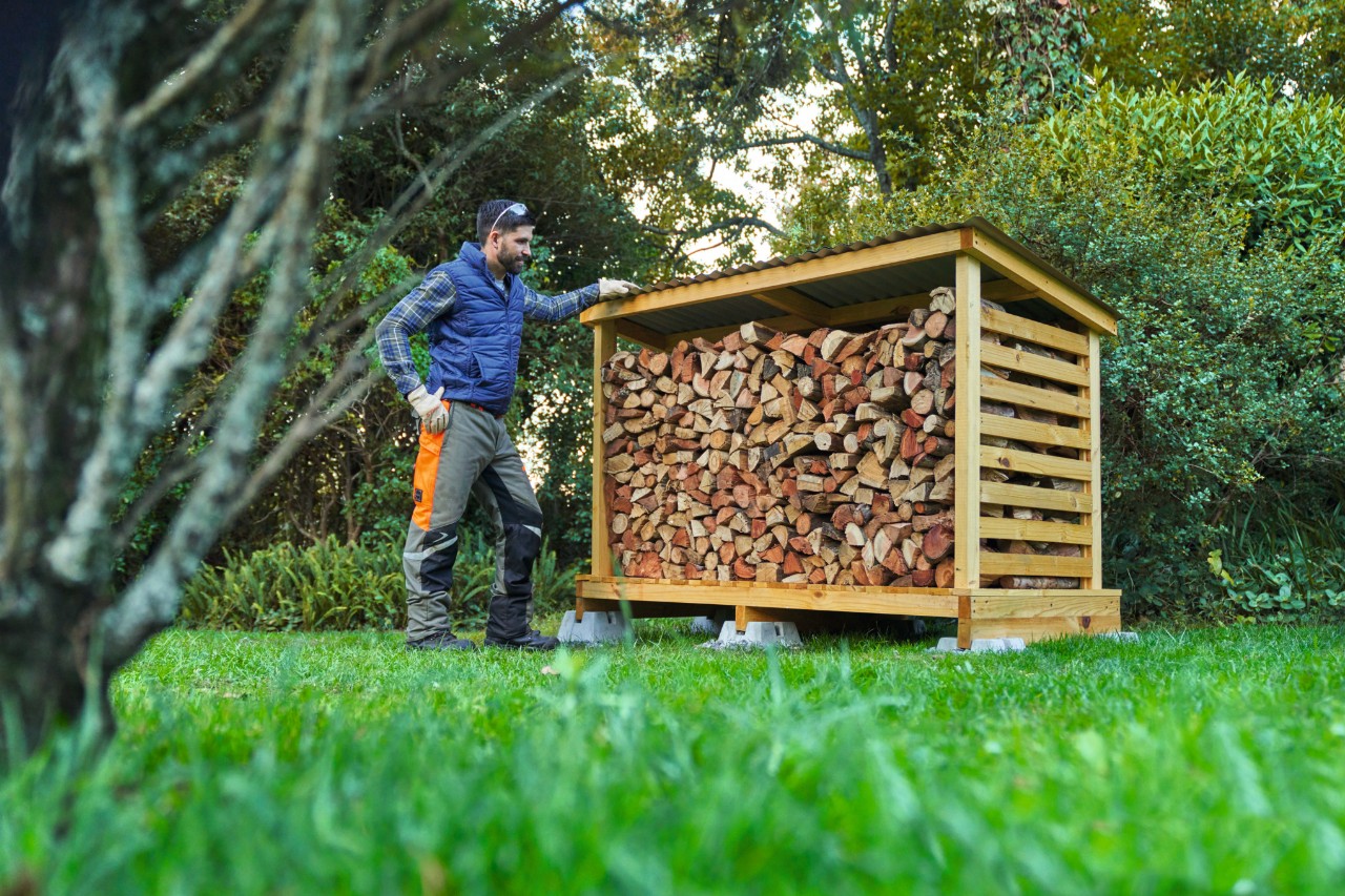 Un hombre con equipamiento de protección individual frente a un leñero de construcción propia