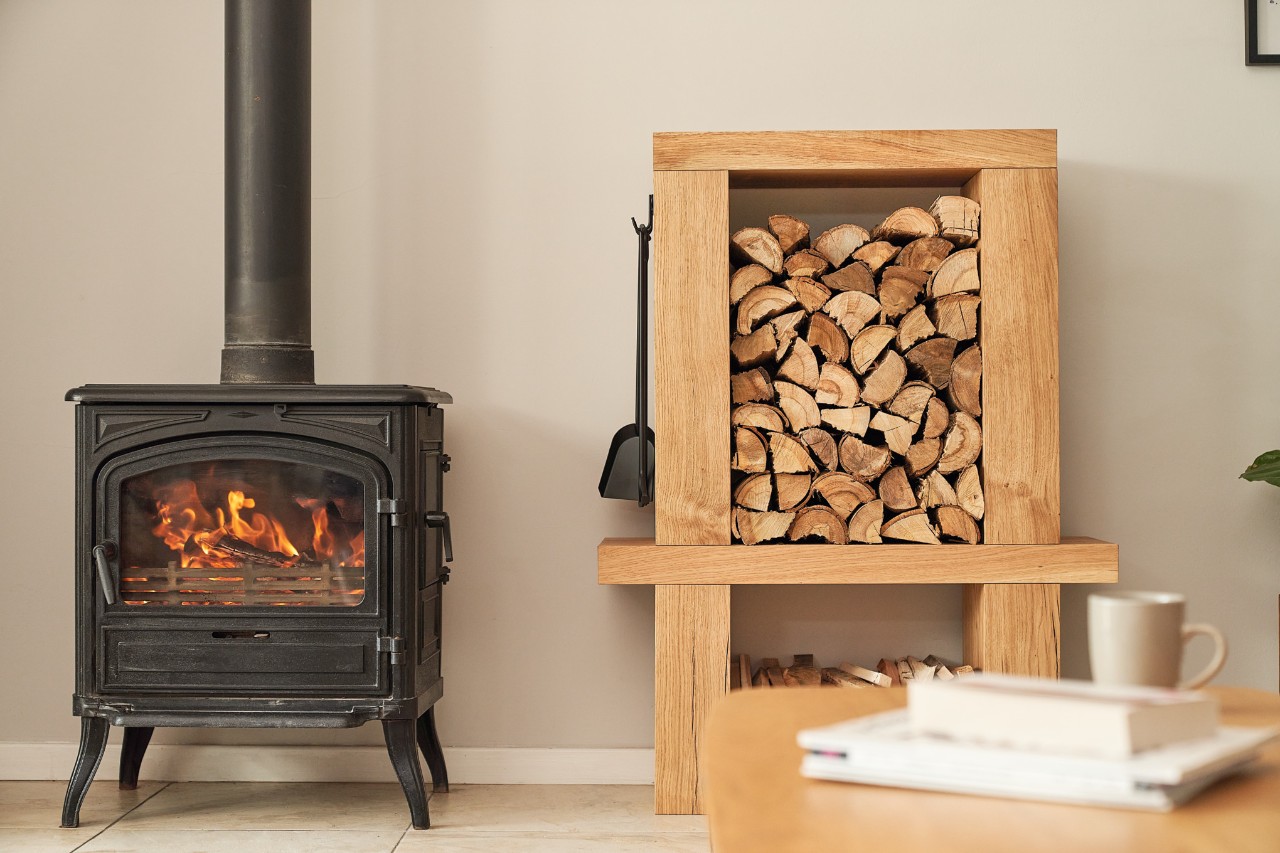 Estantería de leña interior junto a una chimenea encendida