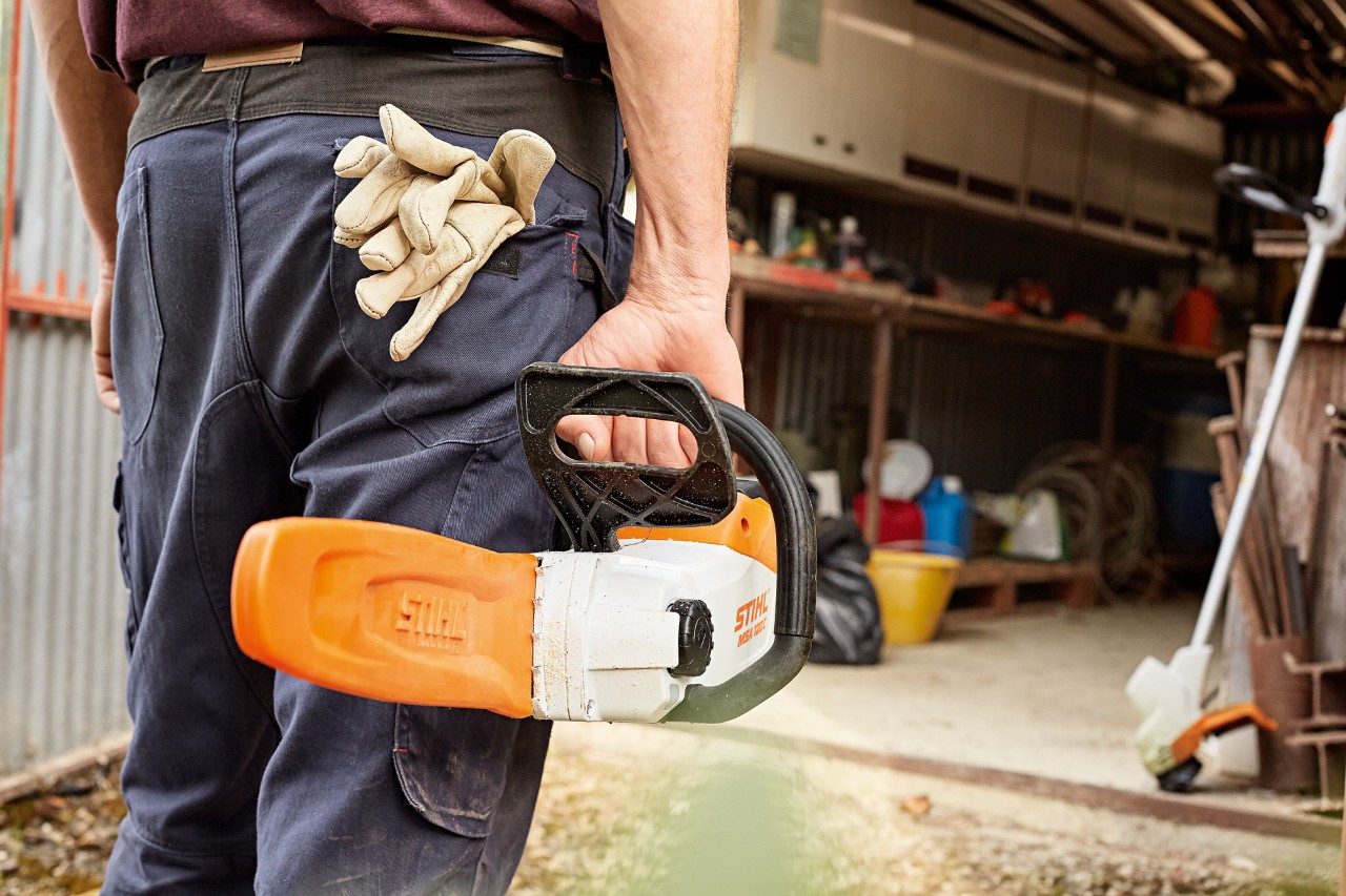 Un hombre entrando en un taller con una motosierra de batería STIHL con funda para la espada