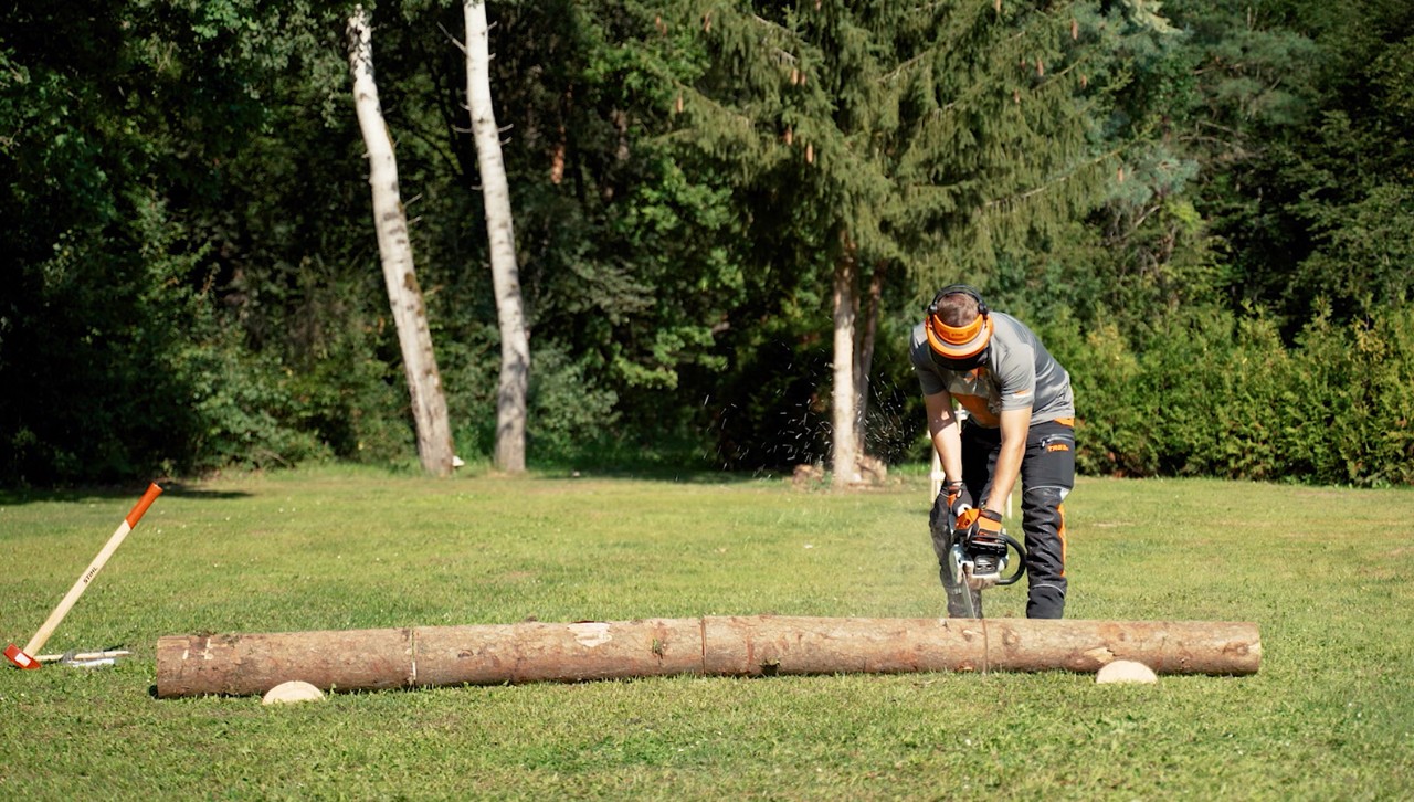 Una persona con equipamiento de protección utiliza una motosierra STIHL para cortar un tronco de árbol para leña.