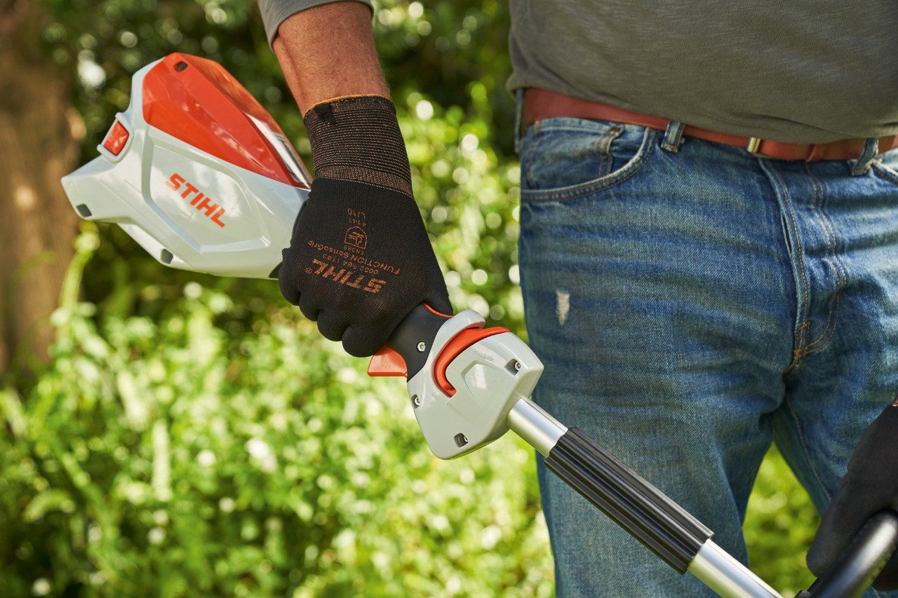 Un hombre con guantes de protección presiona el bloqueo de la palanca multifunción de la desbrozadora de batería STIHL FSA 60 