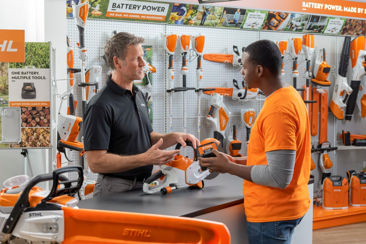 un distribuidor STIHL aconseja a un hombre durante la compra de una motosierra STIHL delante de las estanterías de la tienda