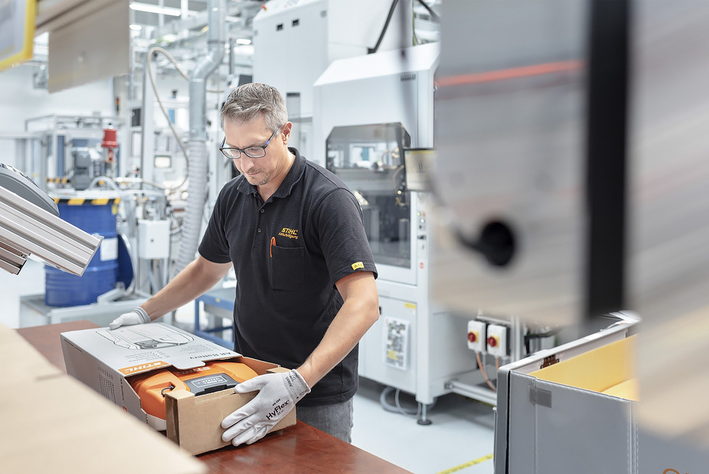 Un hombre con guantes de trabajo introduce cuidadosamente una batería profesional en una caja de cartón